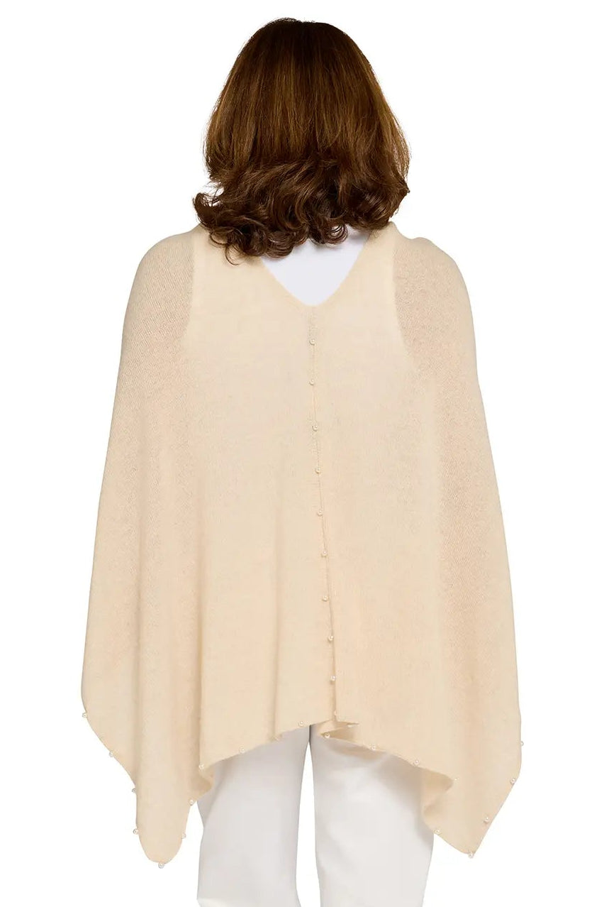Woman wearing a beige poncho over a white top and pants on a white background