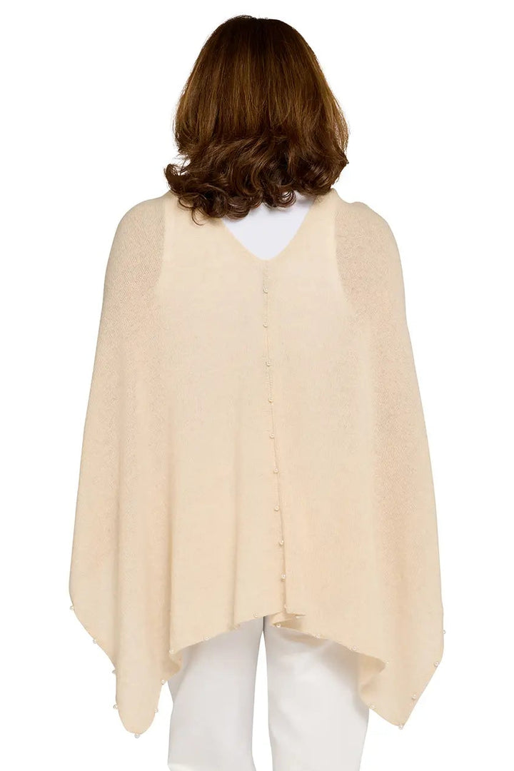 Woman wearing a beige poncho over a white top and pants on a white background