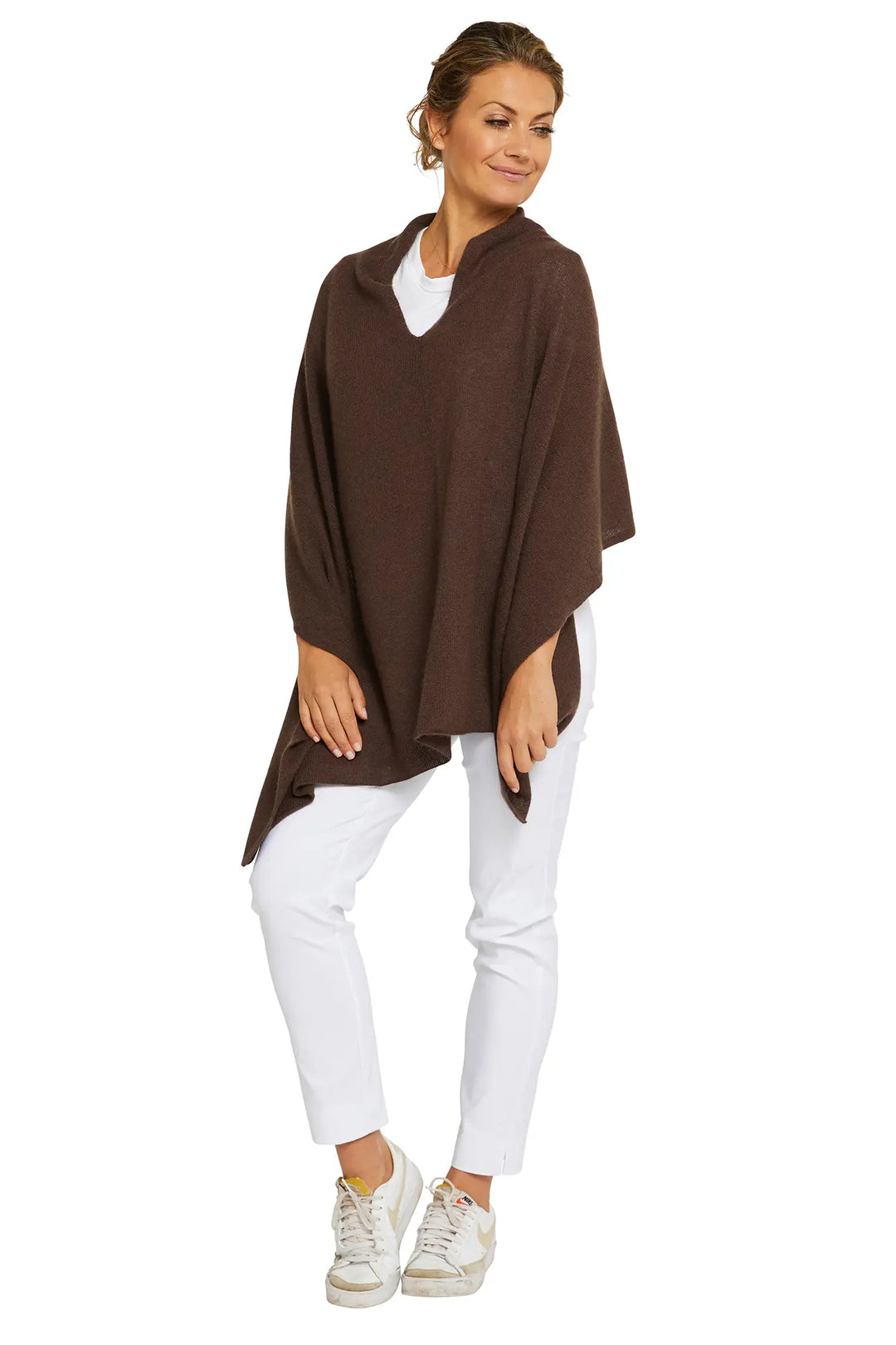 Woman wearing a brown poncho over a white top and pants on a white background