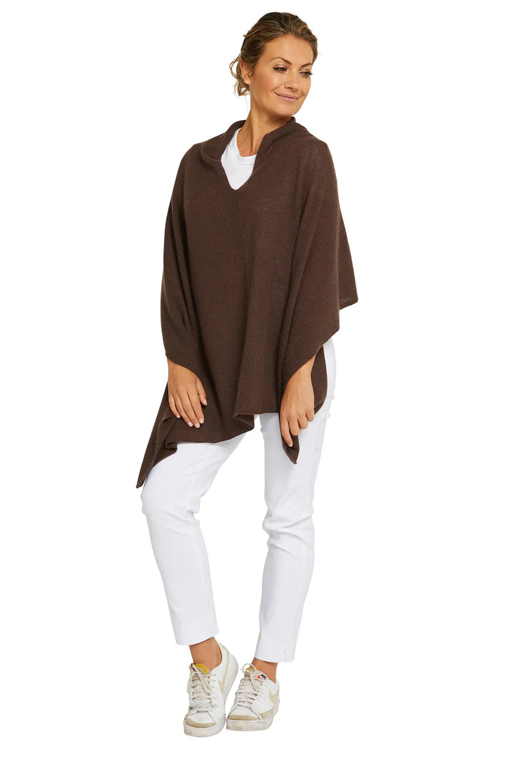 Woman wearing a brown poncho over a white top and pants on a white background