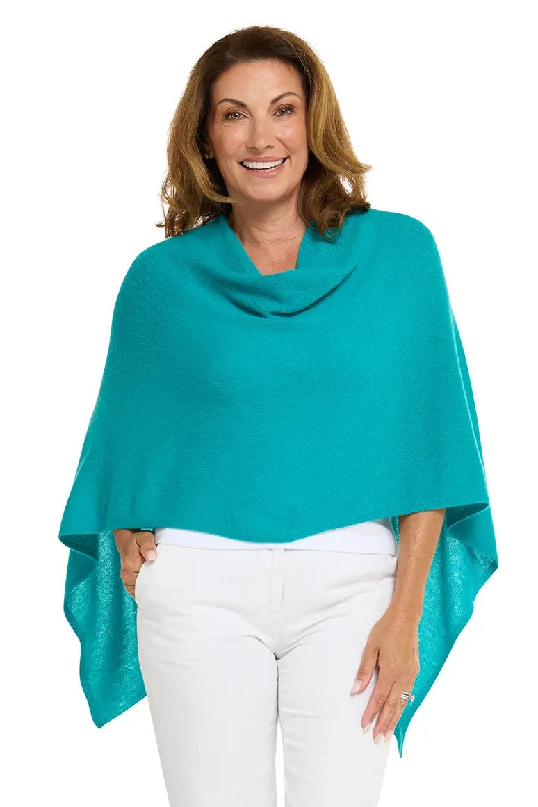 Woman wearing a teal poncho and white pants on a white background