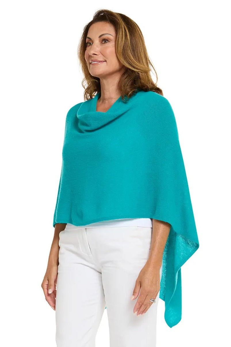 Woman wearing a teal poncho over a white top and pants on a white background