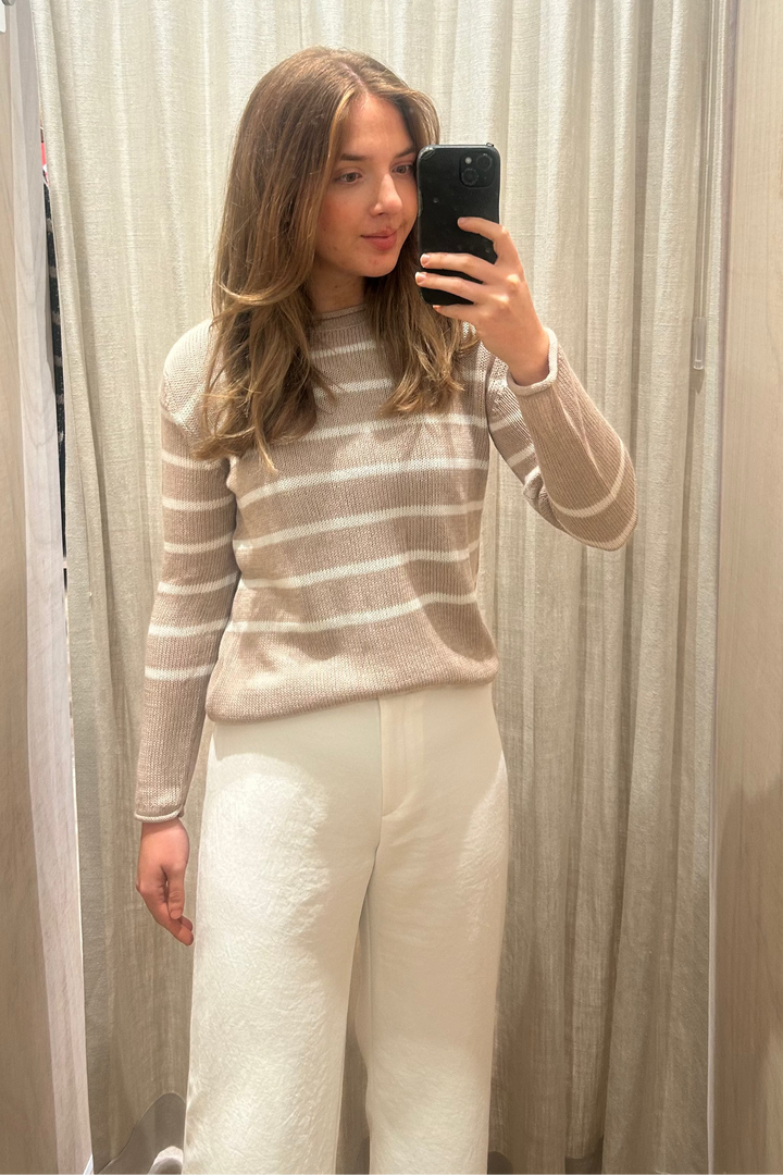 Person taking a mirror selfie wearing a striped sweater and white pants in a fitting room.