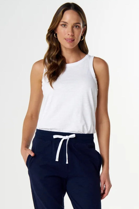 A woman modeling navy blue jogger pants with a white drawstring, paired with a white sleeveless top and white slide sandals, against a plain white studio background.
