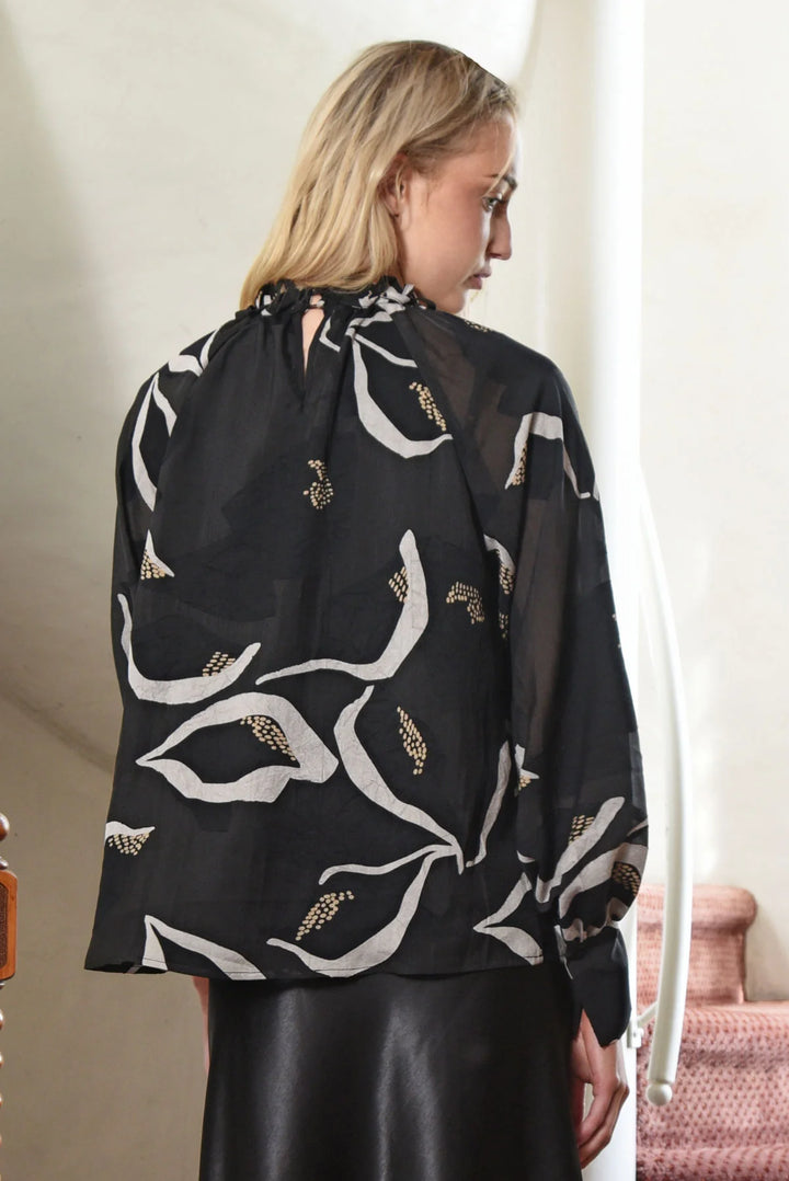 Woman wearing a black blouse with white floral patterns in a minimal indoor setting