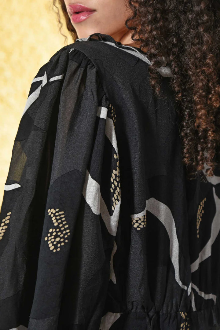 Black garment with white and gold patterns worn by a person with curly hair.
