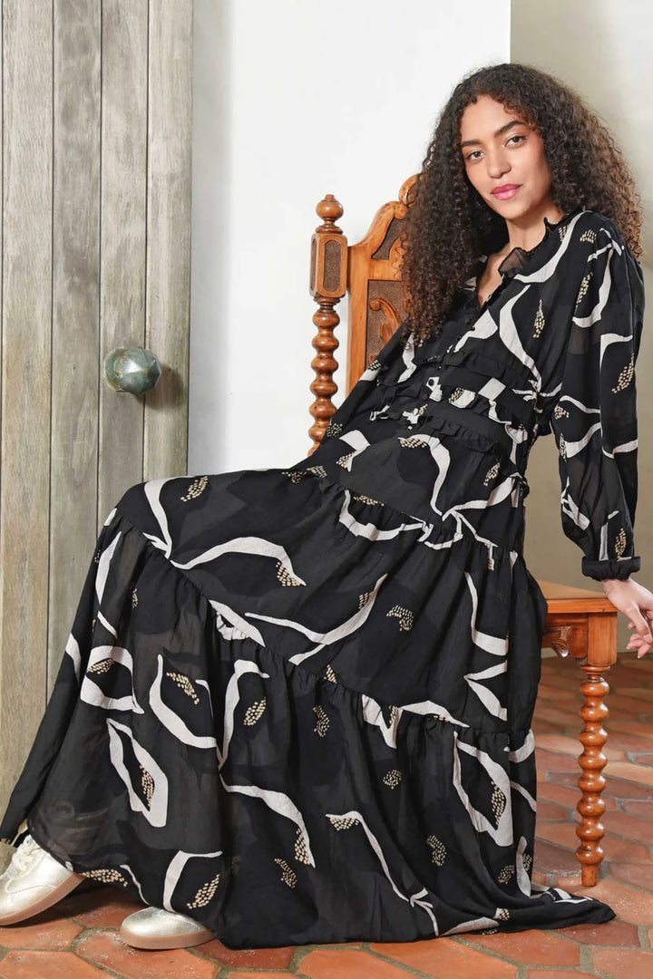 Woman wearing a black dress with white patterns sitting on a wooden chair.