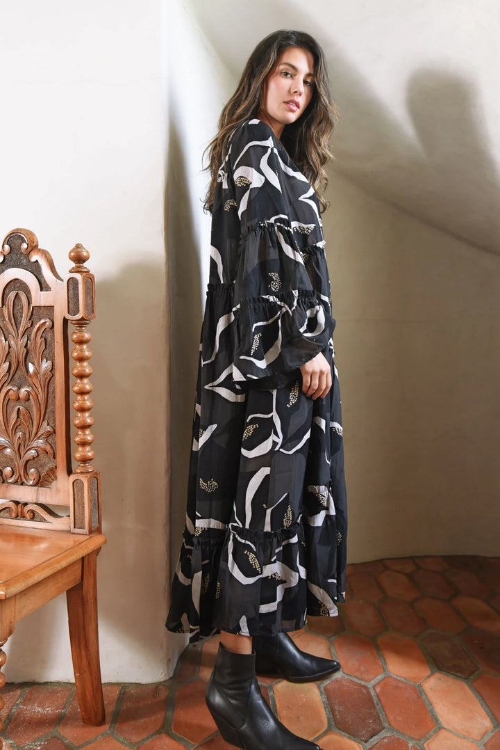 Woman wearing a black and white patterned dress standing against a white wall.