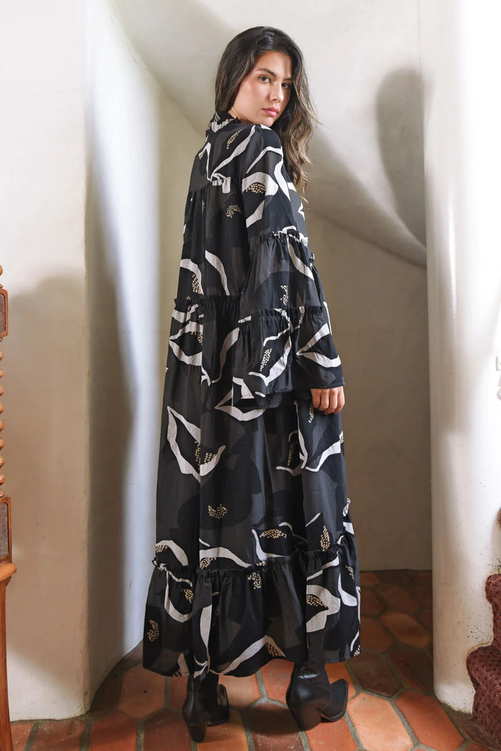 Woman wearing a long, dark blue dress with white patterns in an indoor setting.