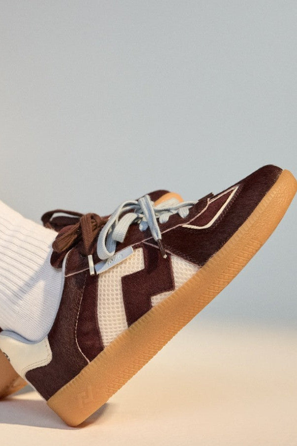 Brown and white patterned sneakers with brown soles worn with white socks and blue jeans.