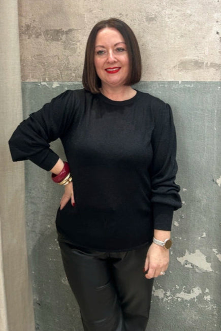 Woman in a black outfit standing against a textured wall.