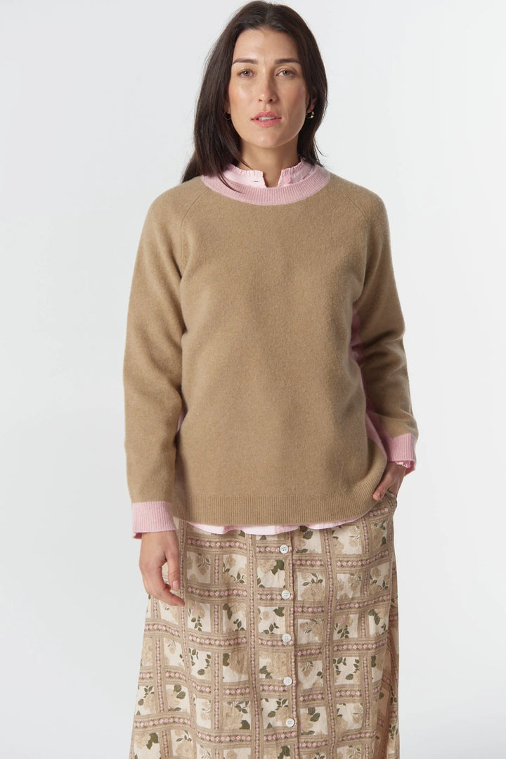 Woman wearing a beige sweater over a pink shirt with a patterned skirt on a white background