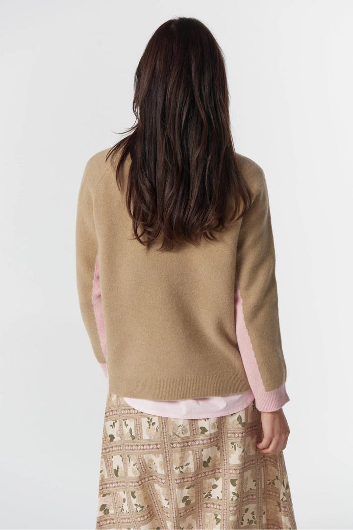 Person wearing a beige sweater with pink sleeves and a patterned skirt on a white background