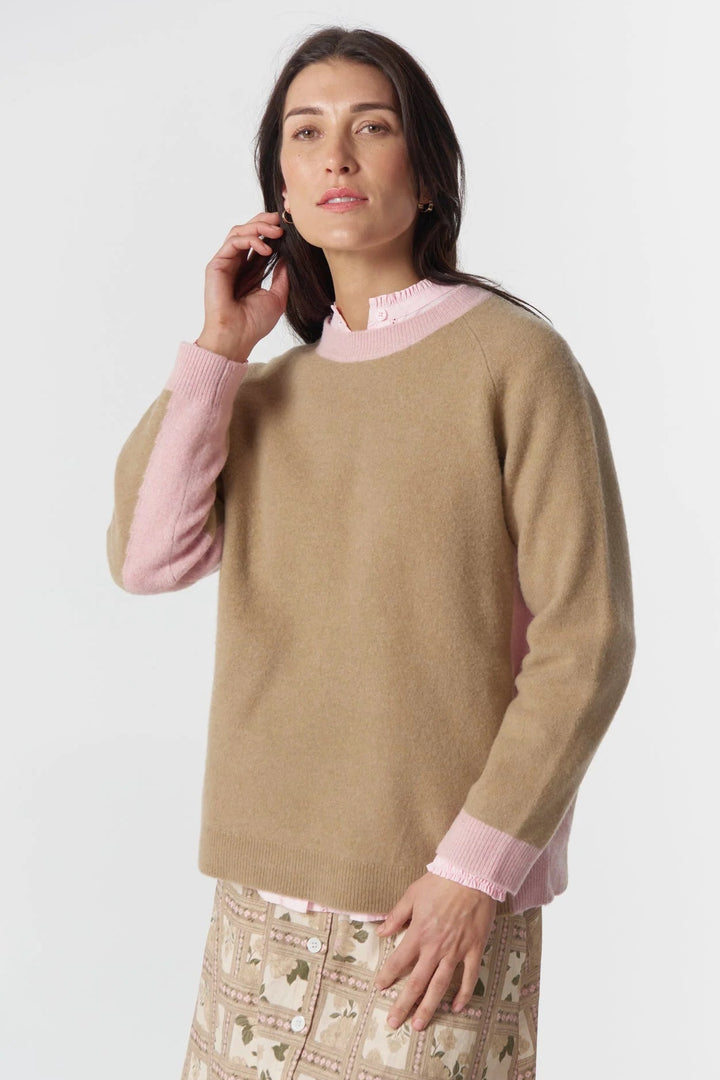 Woman wearing a beige sweater over a pink shirt with a white background