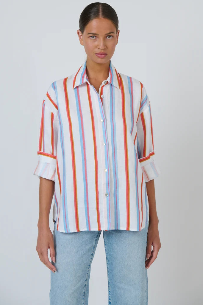 A woman modeling a white button-up shirt with vertical red, orange, and blue stripes, paired with light-wash blue jeans, against a plain light gray background.