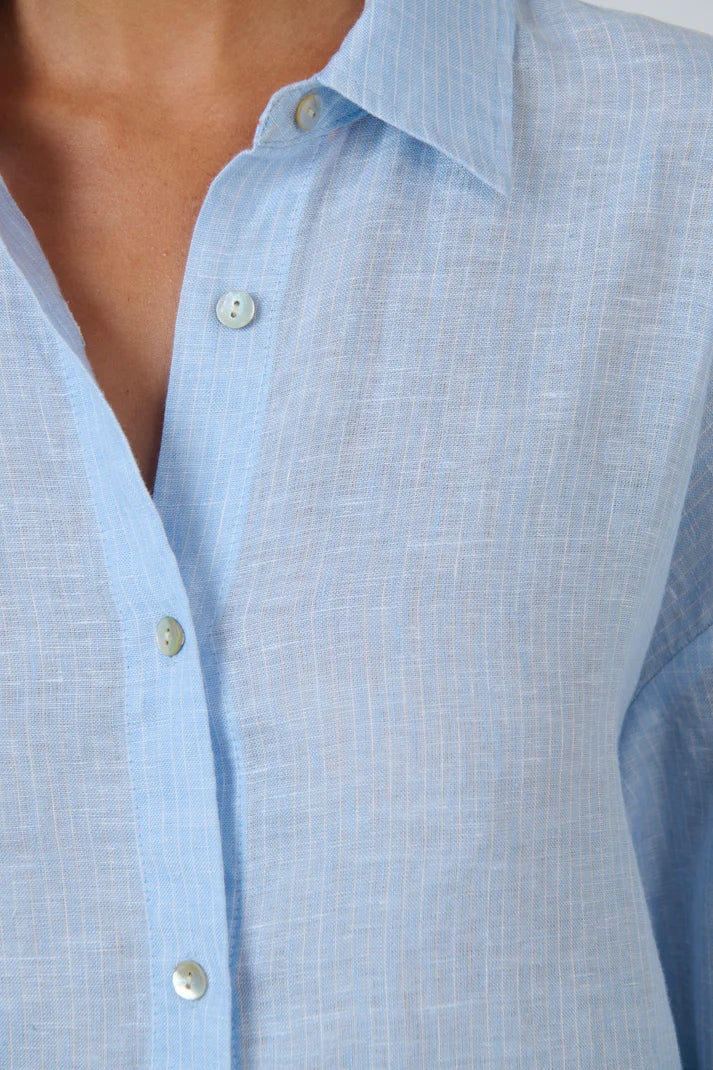 Close-up of a light blue linen button-down shirt worn by a model, showing the collar, buttons, and textured fabric.