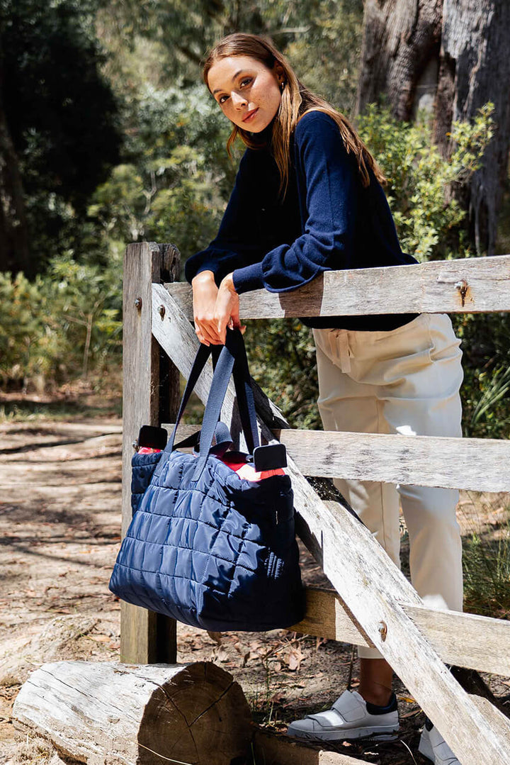 Woman holding a blue quilted bag outdoors near a wooden fence.