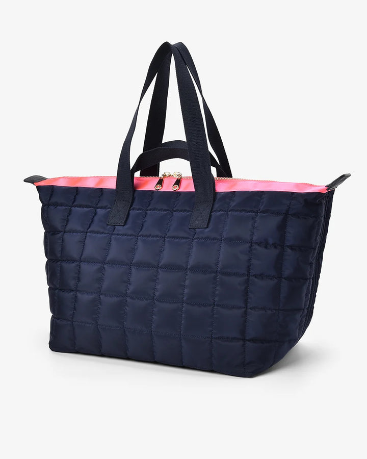 Navy quilted tote bag with black handles and pink interior on a white background