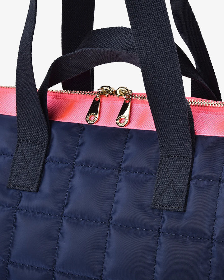 Navy blue quilted bag with a pink zipper and black straps on a white background