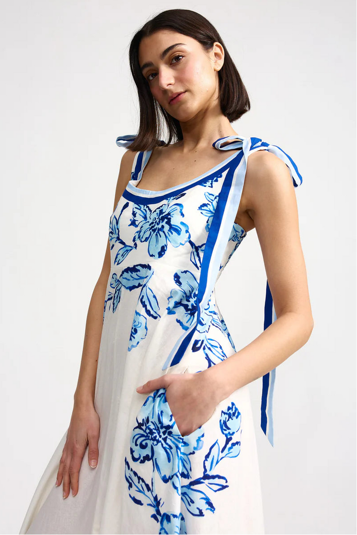 Woman wearing a white dress with blue floral patterns on a plain background