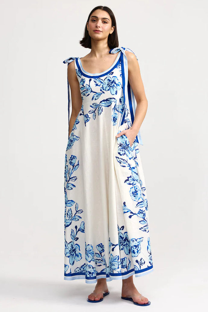 Woman wearing a long white dress with blue floral patterns on a white background