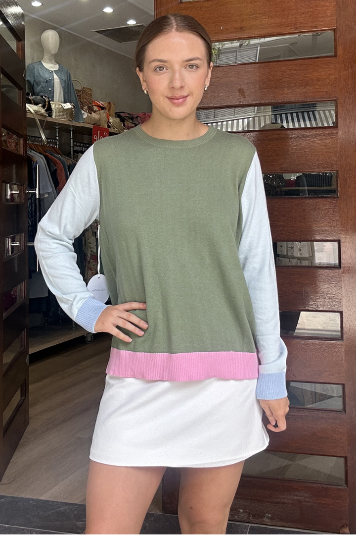 Woman standing in front of a store entrance wearing a green sleeveless top with a white long-sleeve shirt underneath, pink trim, and a white skirt.