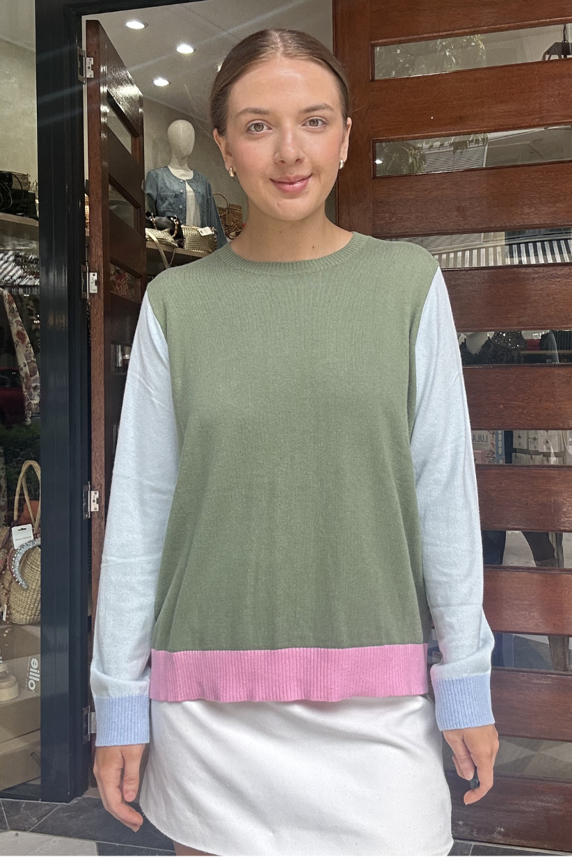 Woman wearing a green and pink top with a white skirt standing in front of a store entrance.