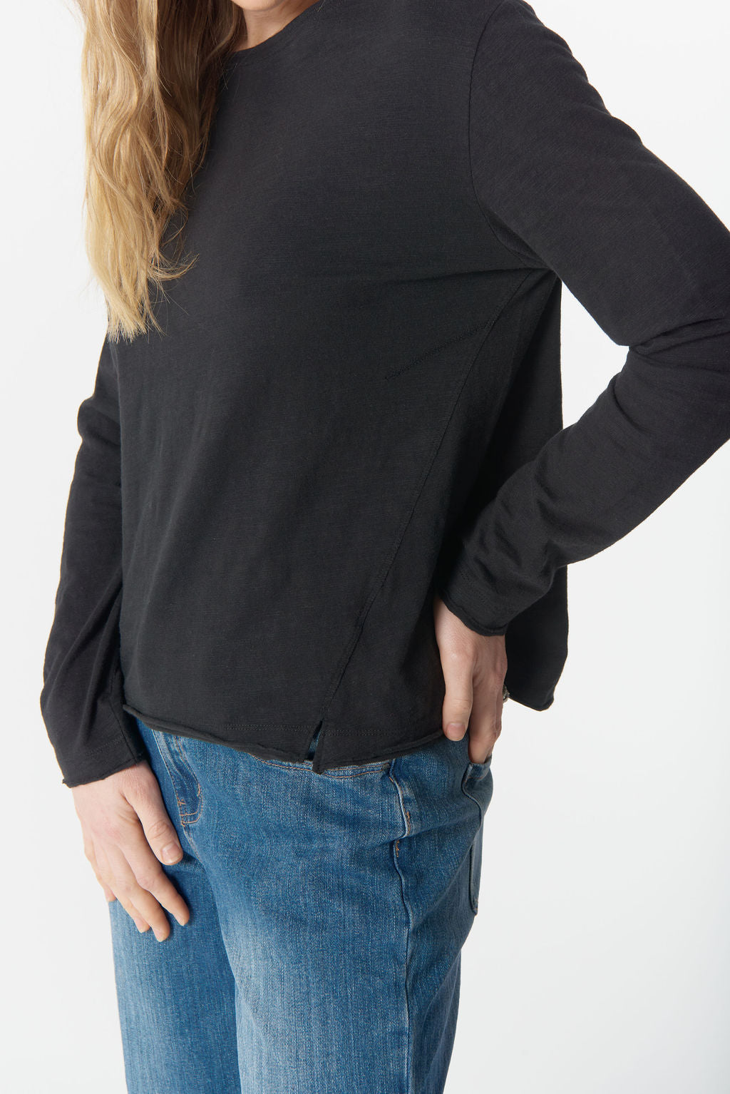 Person wearing a black long-sleeve top and blue jeans on a white background