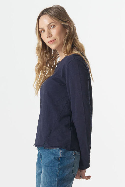 Woman wearing a navy sweater and blue jeans standing against a white background