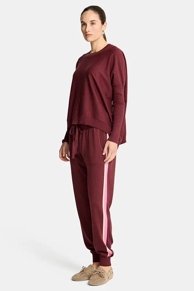 Person wearing a burgundy tracksuit with white stripes on a white background