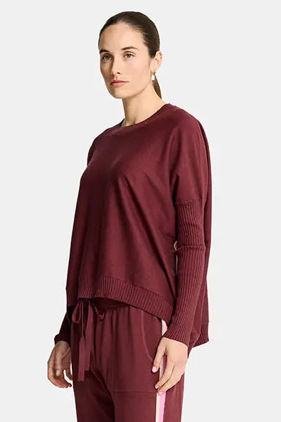 Person wearing a burgundy tracksuit with white stripes on a white background