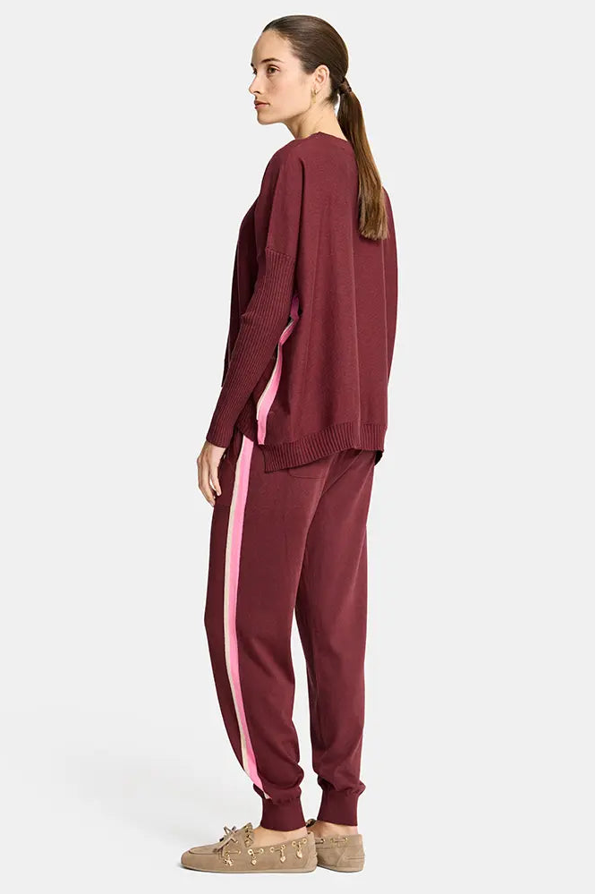 Woman wearing a burgundy tracksuit with pink side stripe on a white background