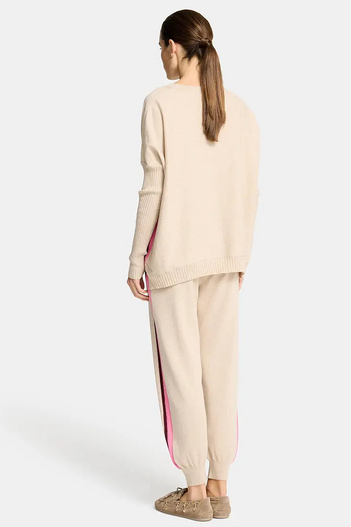 Woman wearing a beige sweater and pants with a pink stripe on a white background