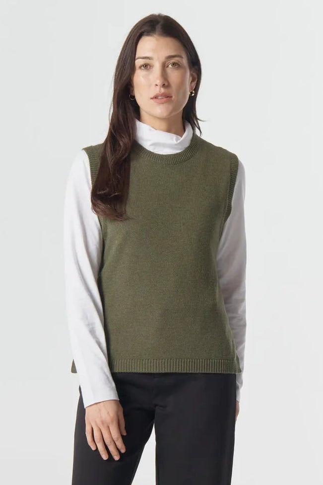 Woman wearing a green sweater, white shirt, black pants, and brown shoes on a white background