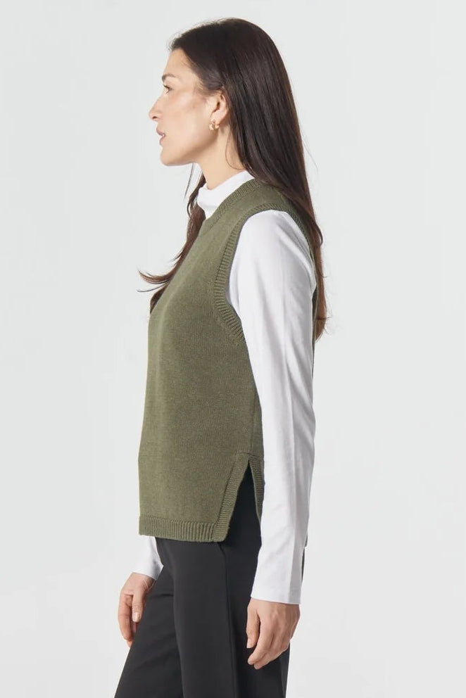Woman wearing a green vest, white shirt, and black pants on a white background
