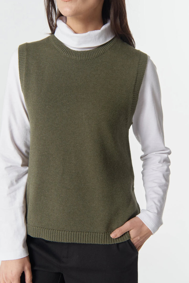 Person wearing a green sweater vest over a white shirt on a white background