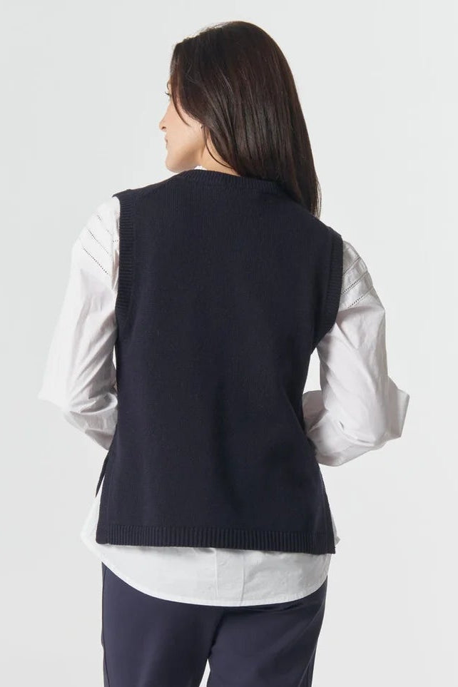 Person wearing a navy vest over a white shirt with dark pants on a white background