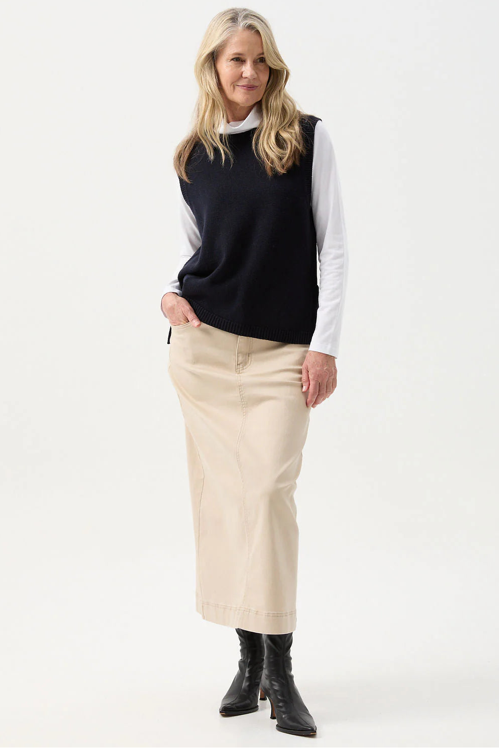 Woman wearing a navy sweater, white shirt, beige skirt, and black boots on a white background