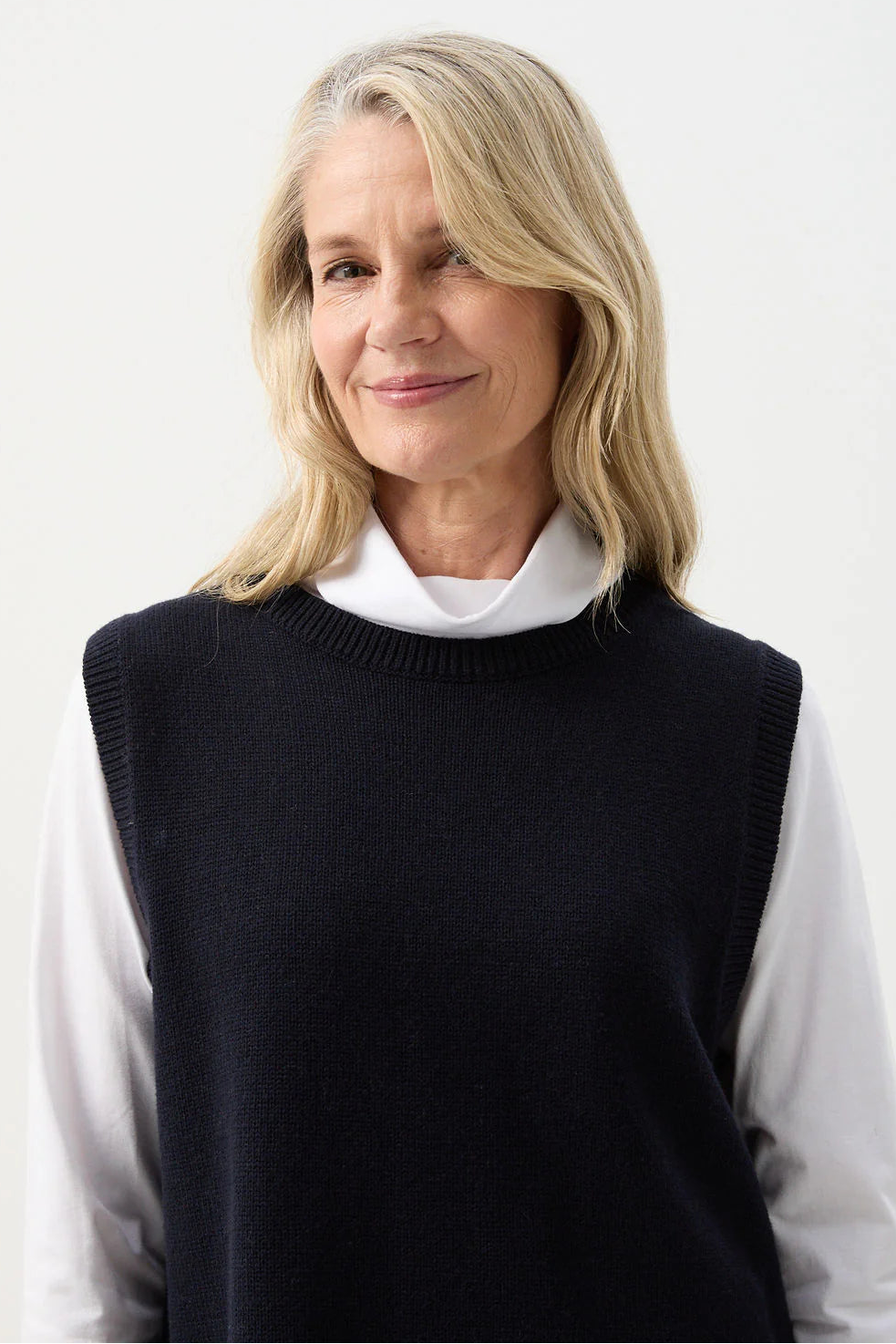 Woman wearing a black vest over a white shirt on a white background