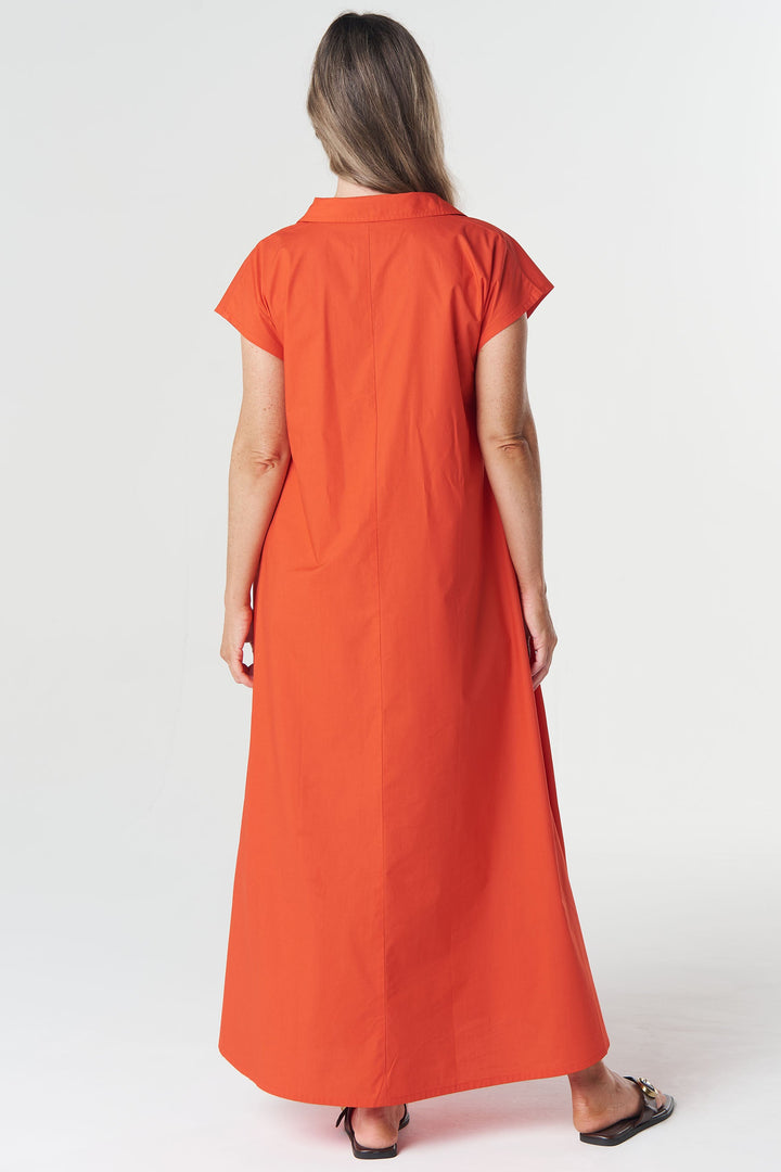 A woman viewed from behind wearing a bright orange short-sleeve maxi dress, standing against a plain light gray studio background.