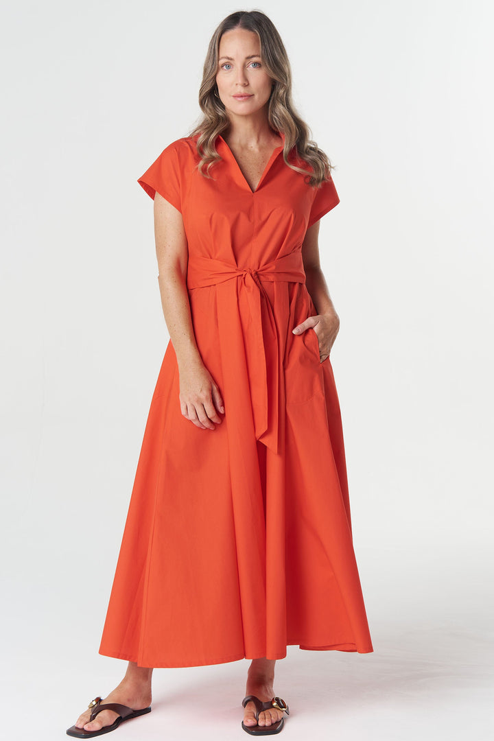 A woman modeling a bright orange wrap-style midi dress with short sleeves, a V-neckline, side pockets, and a self-tie waist, photographed against a clean light gray studio background.