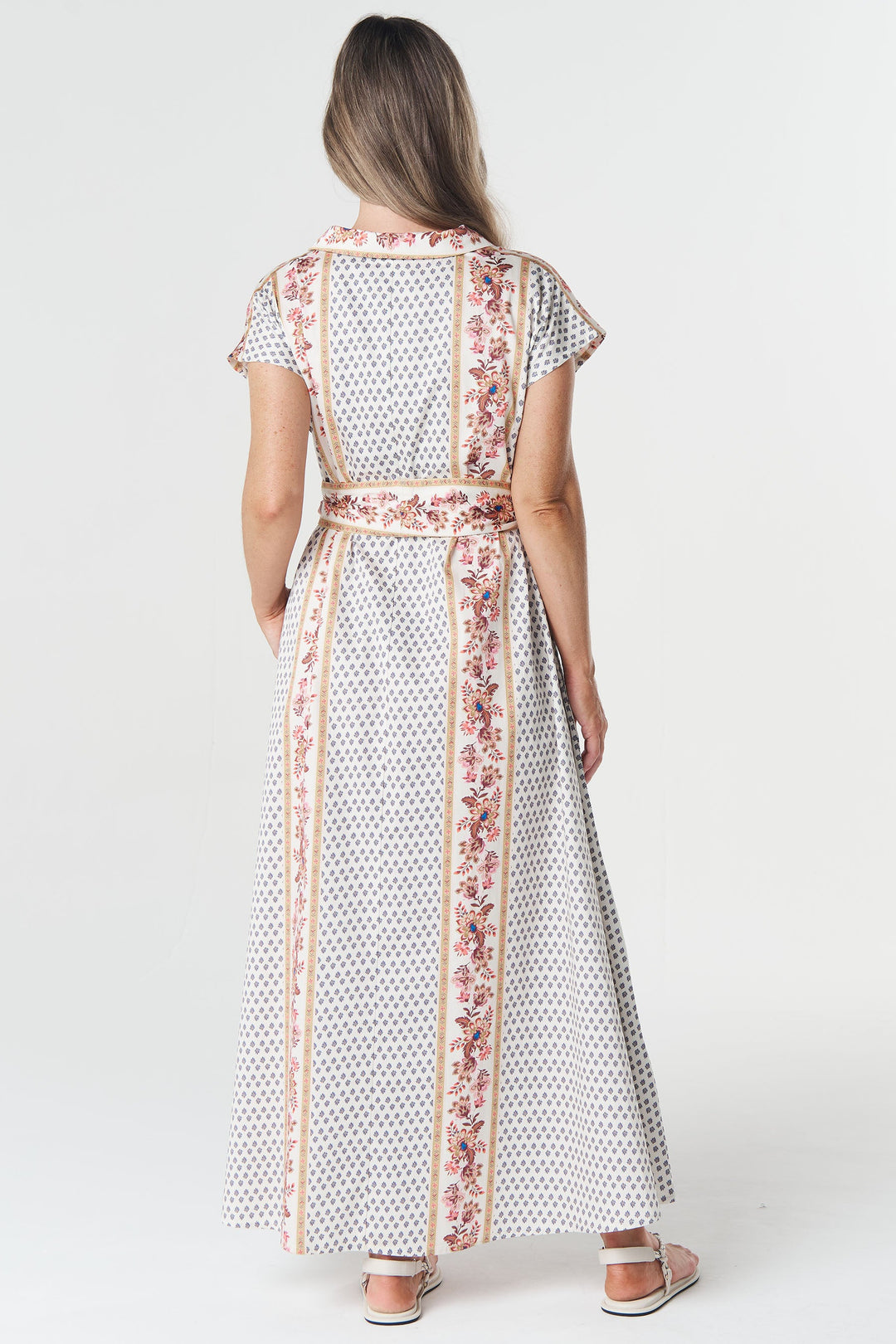 Woman wearing a long, patterned dress with a belt on a white background