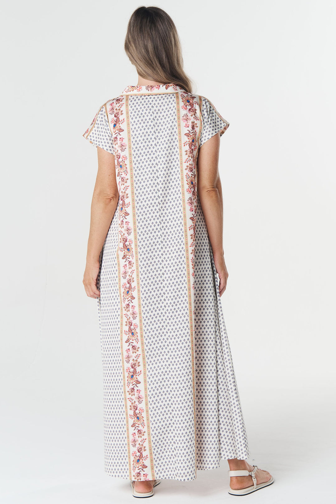 Woman wearing a long, patterned dress with a floral scarf on a white background