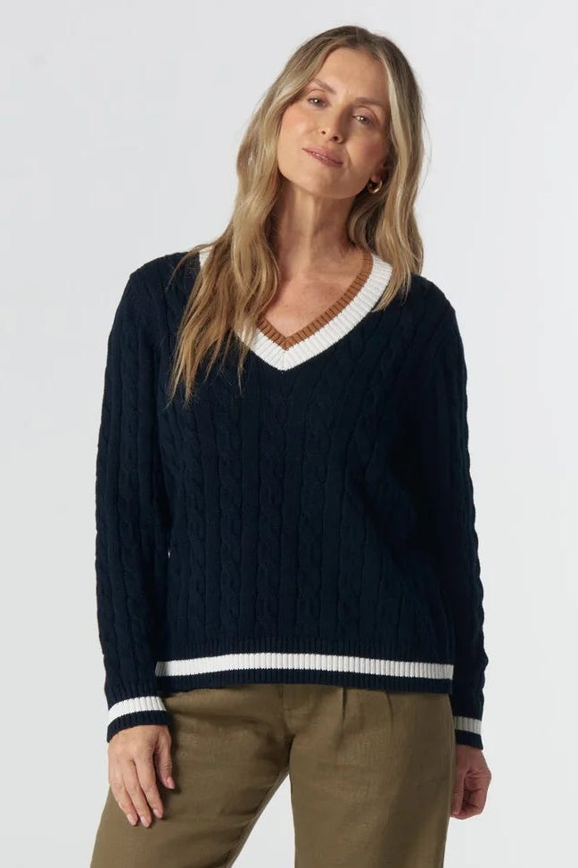 Woman wearing a navy sweater with white trim and beige pants on a white background