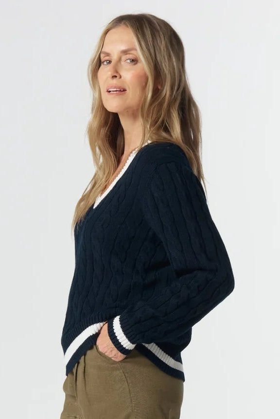 Woman wearing a navy sweater with white trim and beige pants on a white background