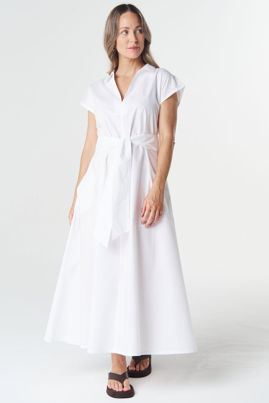 A woman modeling a white short-sleeve midi dress with a tie waist, standing against a seamless white studio background.