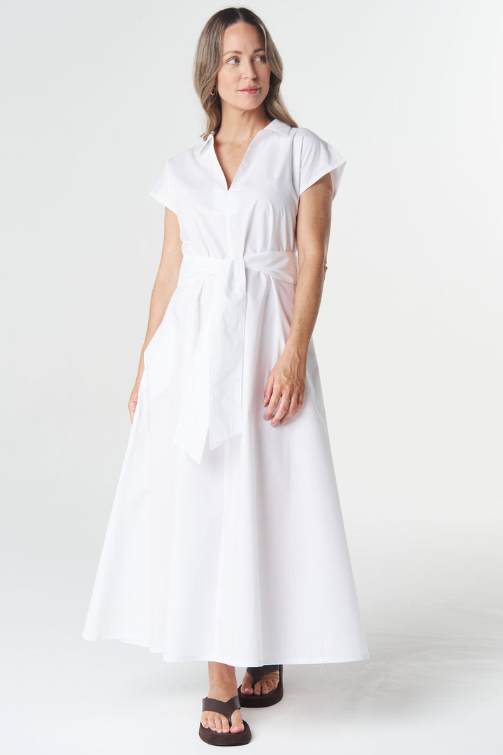 A woman modeling a white short-sleeve midi dress with a tie waist, standing against a seamless white studio background.