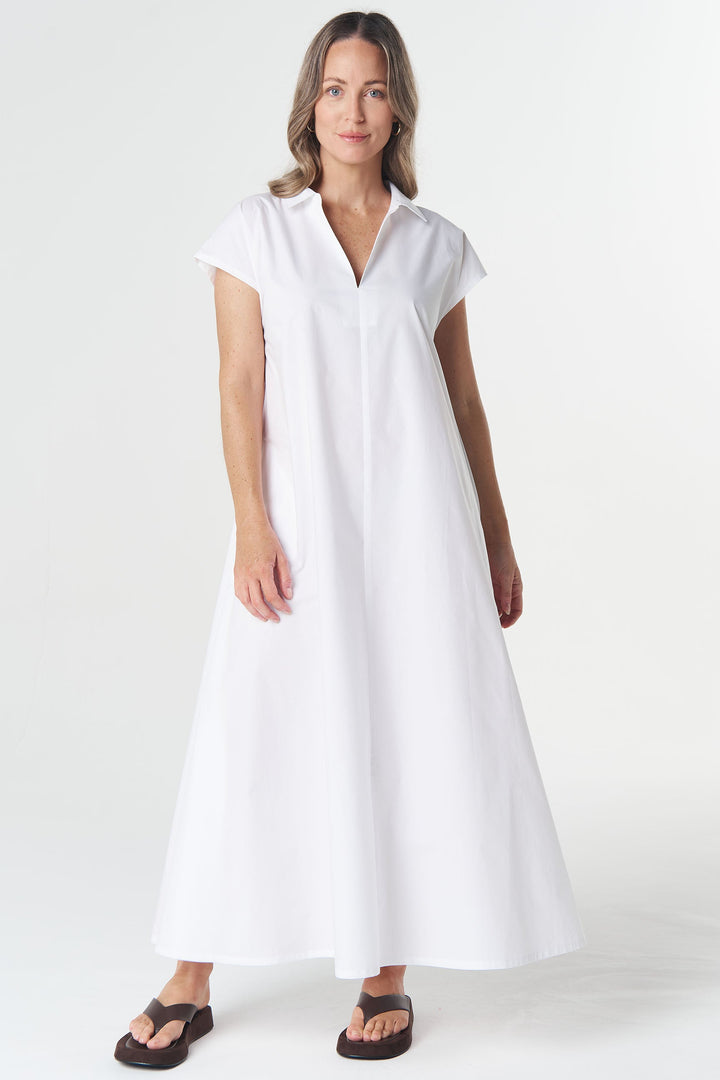 A woman modeling a white short-sleeve maxi dress with a V-neckline, standing against a seamless white studio background.