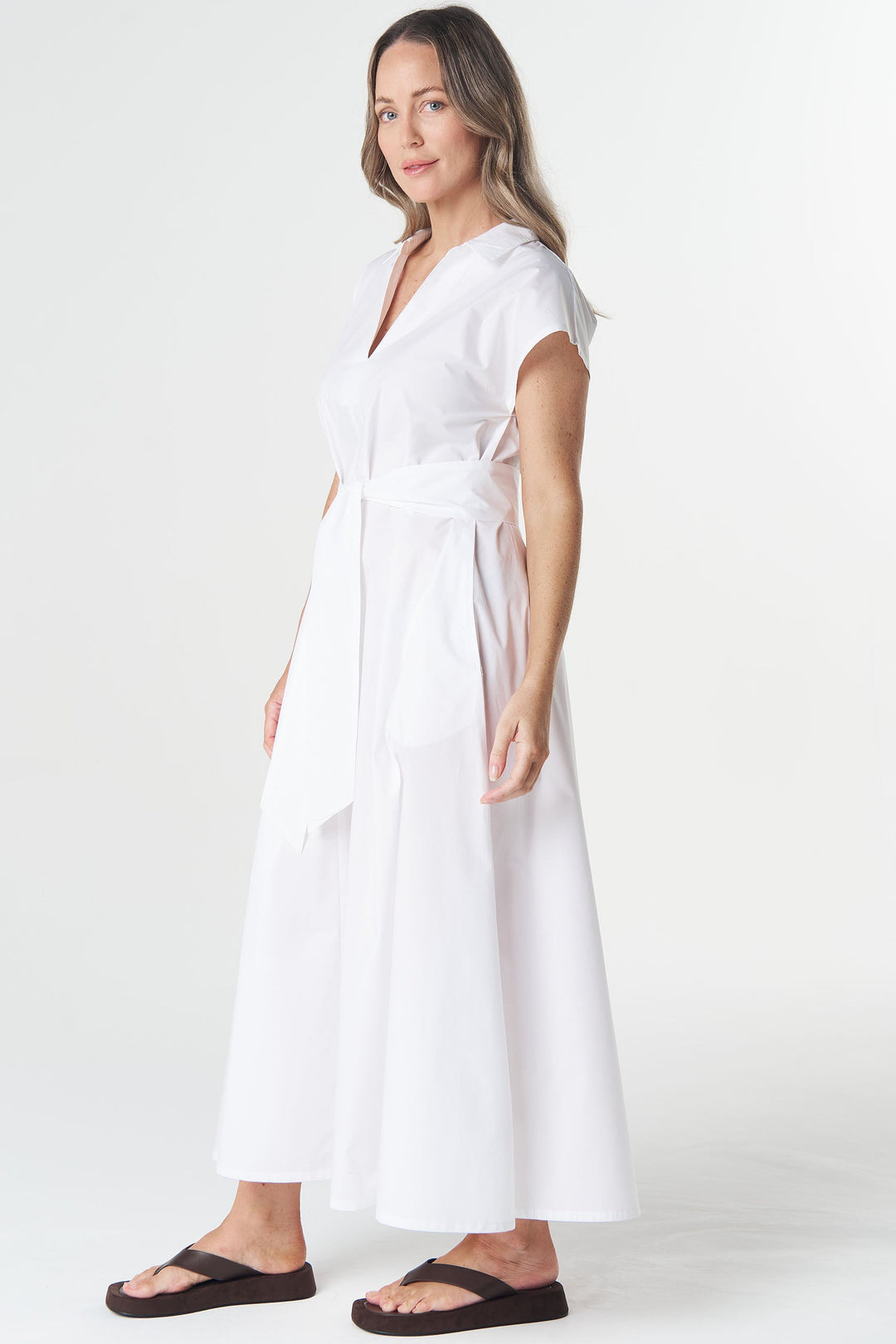 A woman modeling a white short-sleeve midi wrap dress with a tie waist, standing against a plain white studio background.