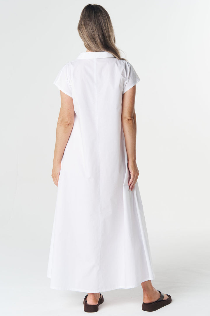 A woman viewed from behind wearing a white short-sleeve collared maxi dress and dark brown sandals, standing against a plain white studio background.